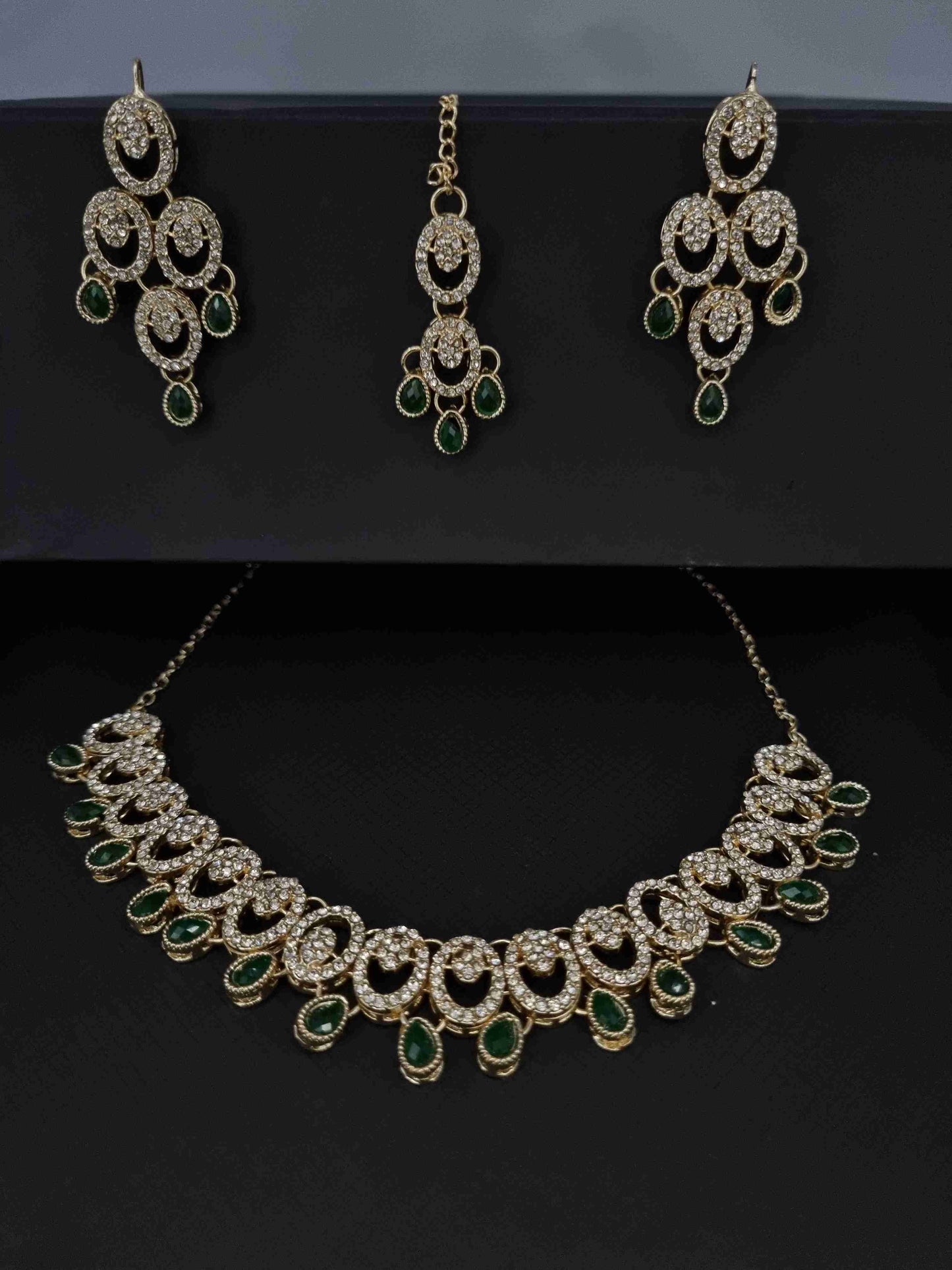 Luxurious green stone and zircon bridal jewelry set featuring an elegant necklace, matching earrings, and a maang tikka.